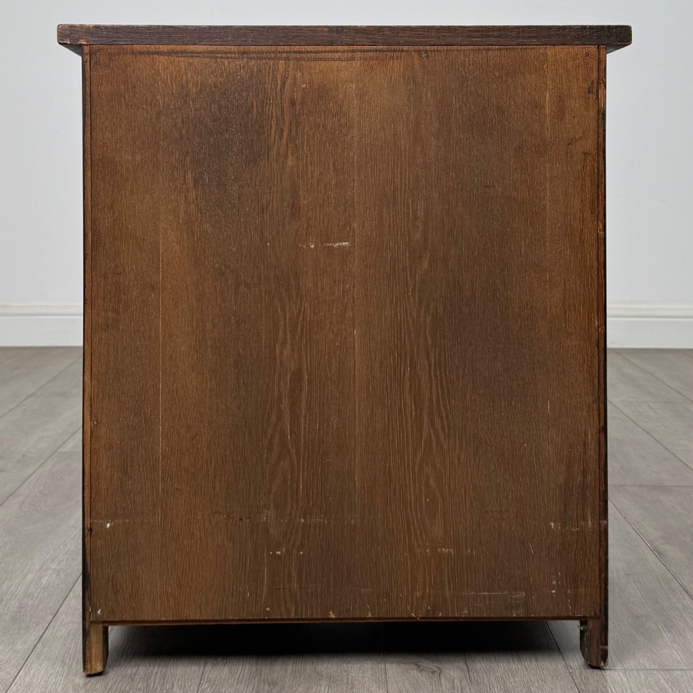 A small early twentieth-century dark oak chest of drawers featuring three drawers with turned wooden knobs and a carved frieze top detail. View V