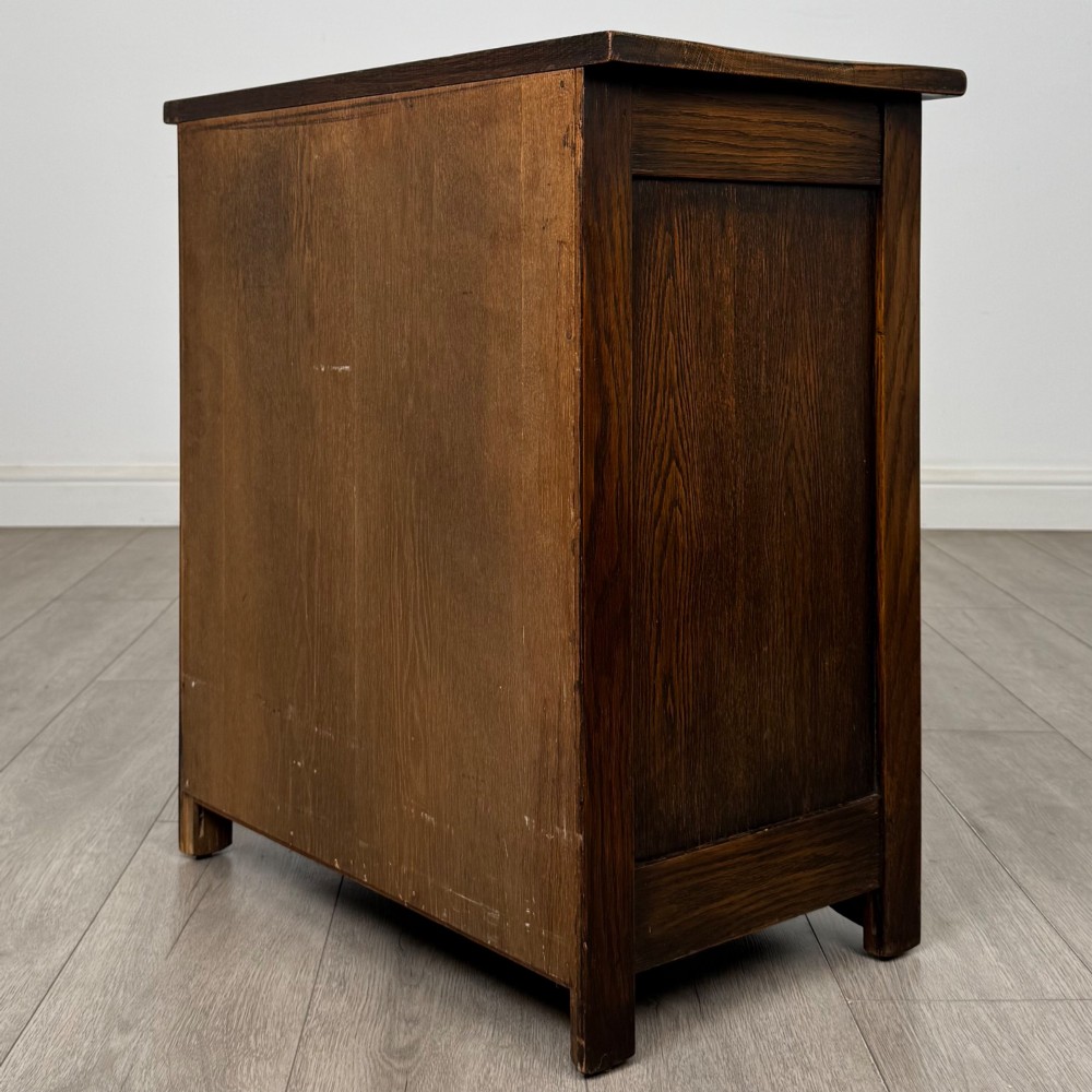 A small early twentieth-century dark oak chest of drawers featuring three drawers with turned wooden knobs and a carved frieze top detail. View VI