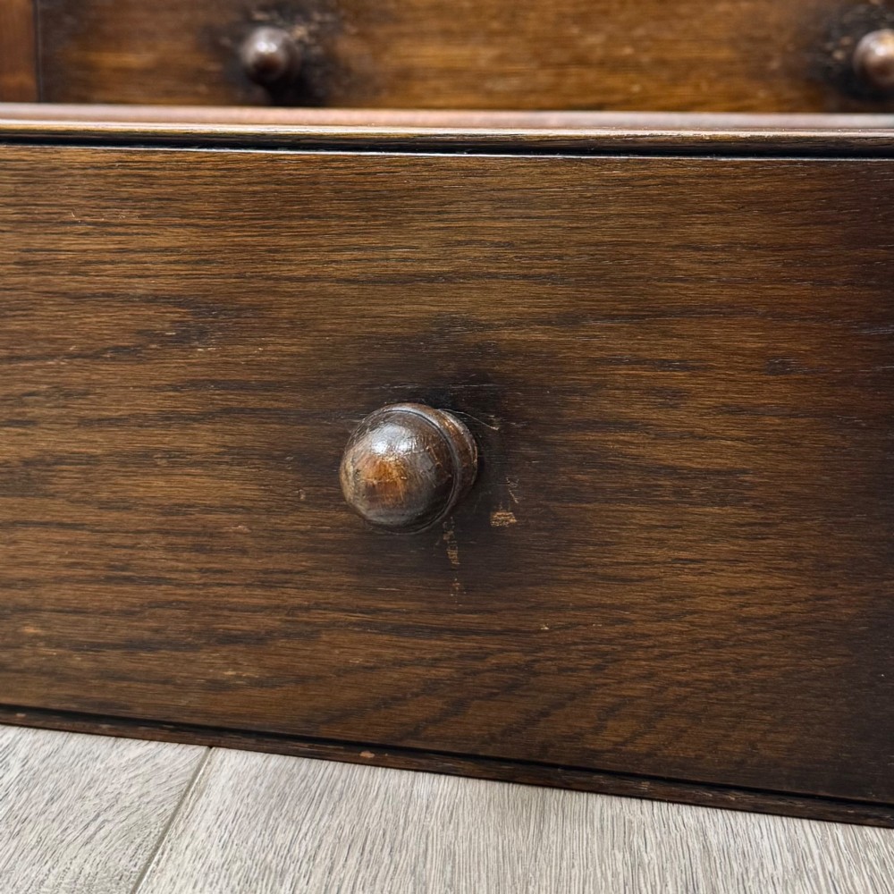 A small early twentieth-century dark oak chest of drawers featuring three drawers with turned wooden knobs and a carved frieze top detail. View XI