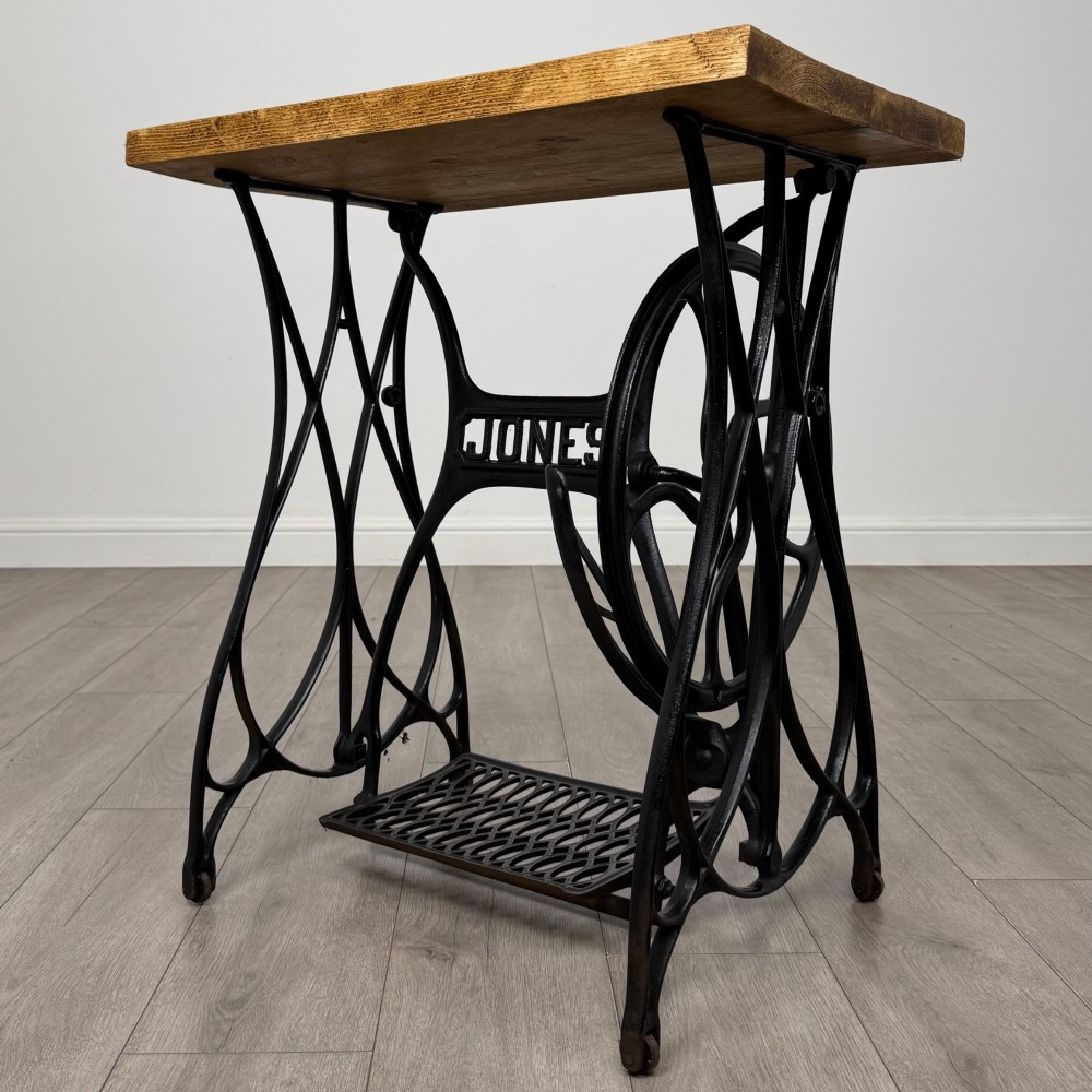 An industrial side table featuring a black cast iron Jones treadle sewing machine base topped with a thick rectangular timber board.