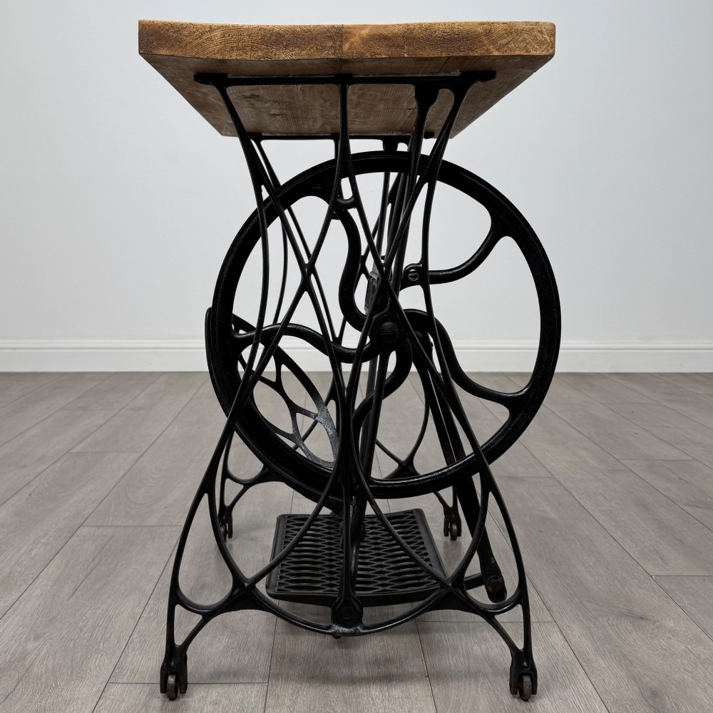 An industrial side table featuring a black cast iron Jones treadle sewing machine base topped with a thick rectangular timber board. View II