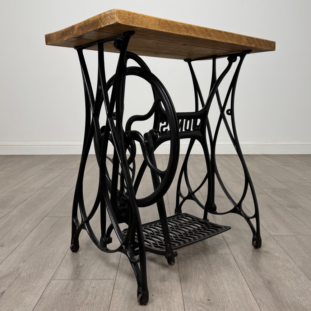 An industrial side table featuring a black cast iron Jones treadle sewing machine base topped with a thick rectangular timber board. View III