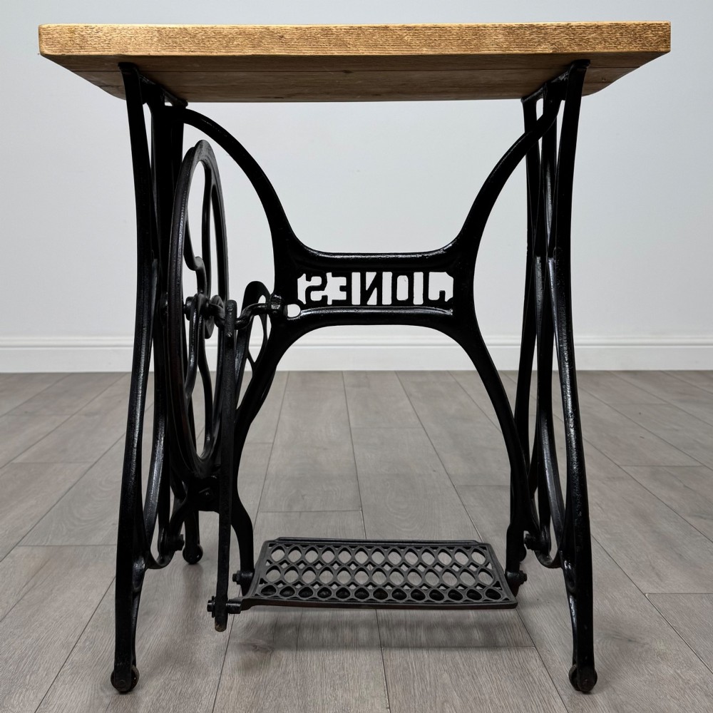 An industrial side table featuring a black cast iron Jones treadle sewing machine base topped with a thick rectangular timber board. View IV