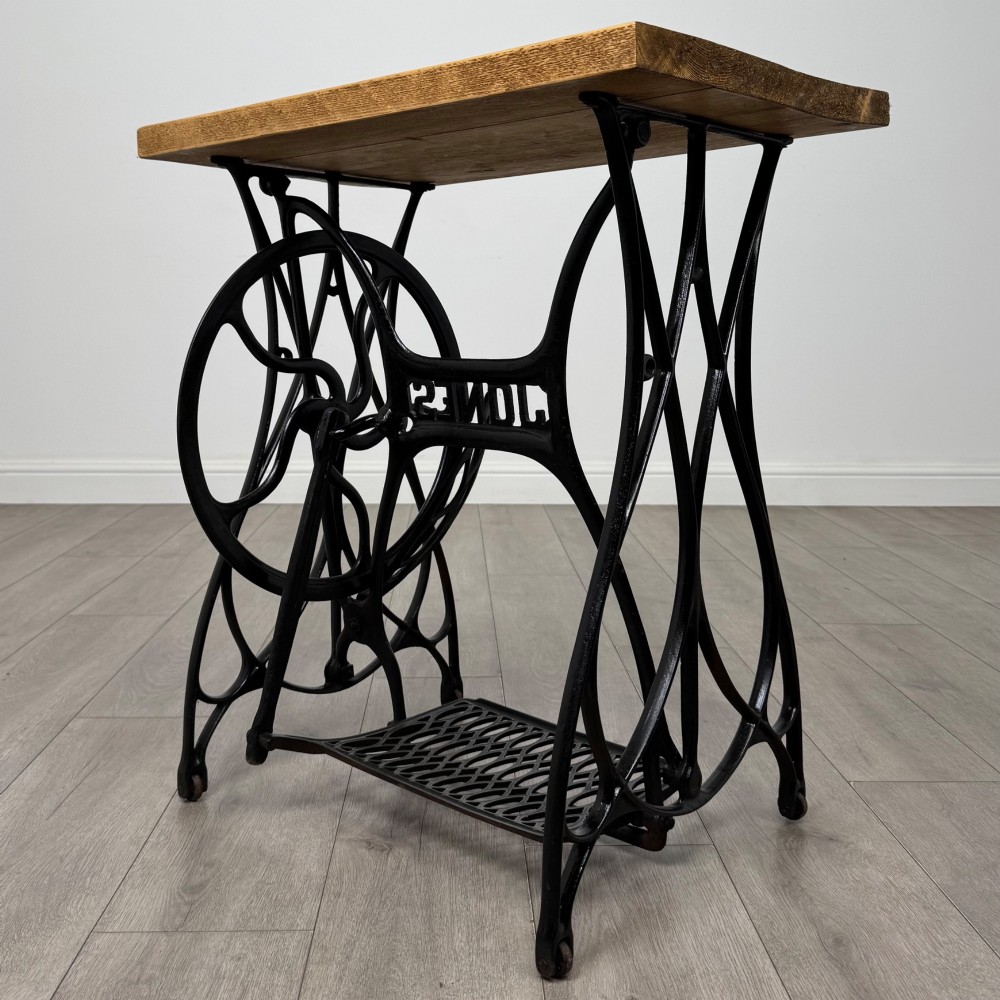 An industrial side table featuring a black cast iron Jones treadle sewing machine base topped with a thick rectangular timber board. View V