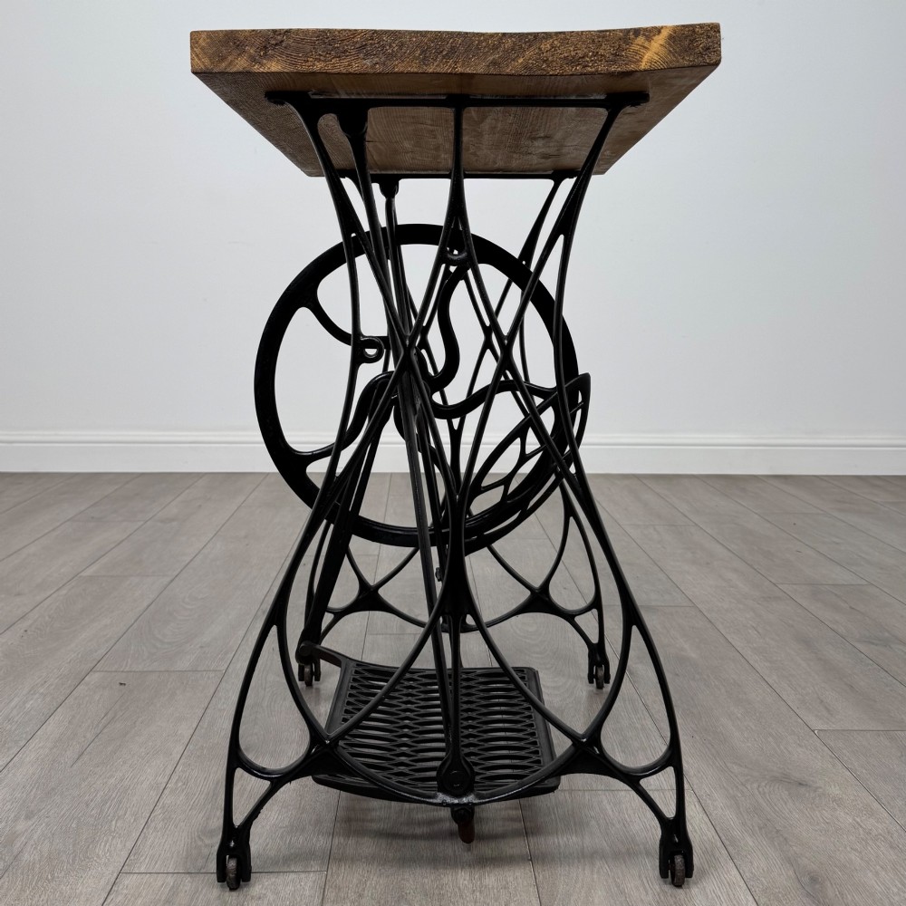 An industrial side table featuring a black cast iron Jones treadle sewing machine base topped with a thick rectangular timber board. View VI