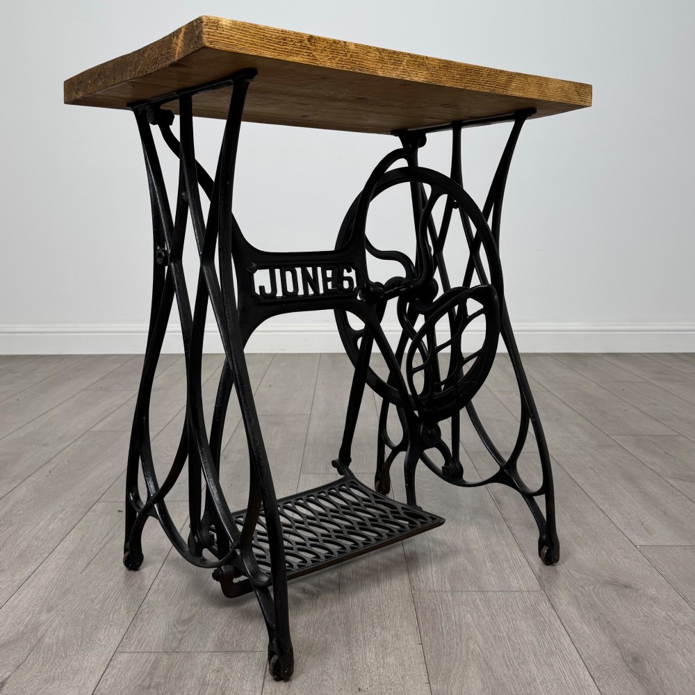 An industrial side table featuring a black cast iron Jones treadle sewing machine base topped with a thick rectangular timber board. View VII