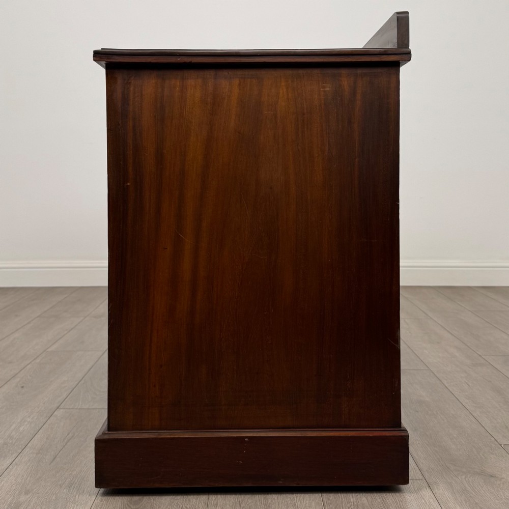 An antique Edwardian walnut pedestal desk featuring nine drawers with reeded panel details, brass drop handles, and a carved kneehole arch. View III
