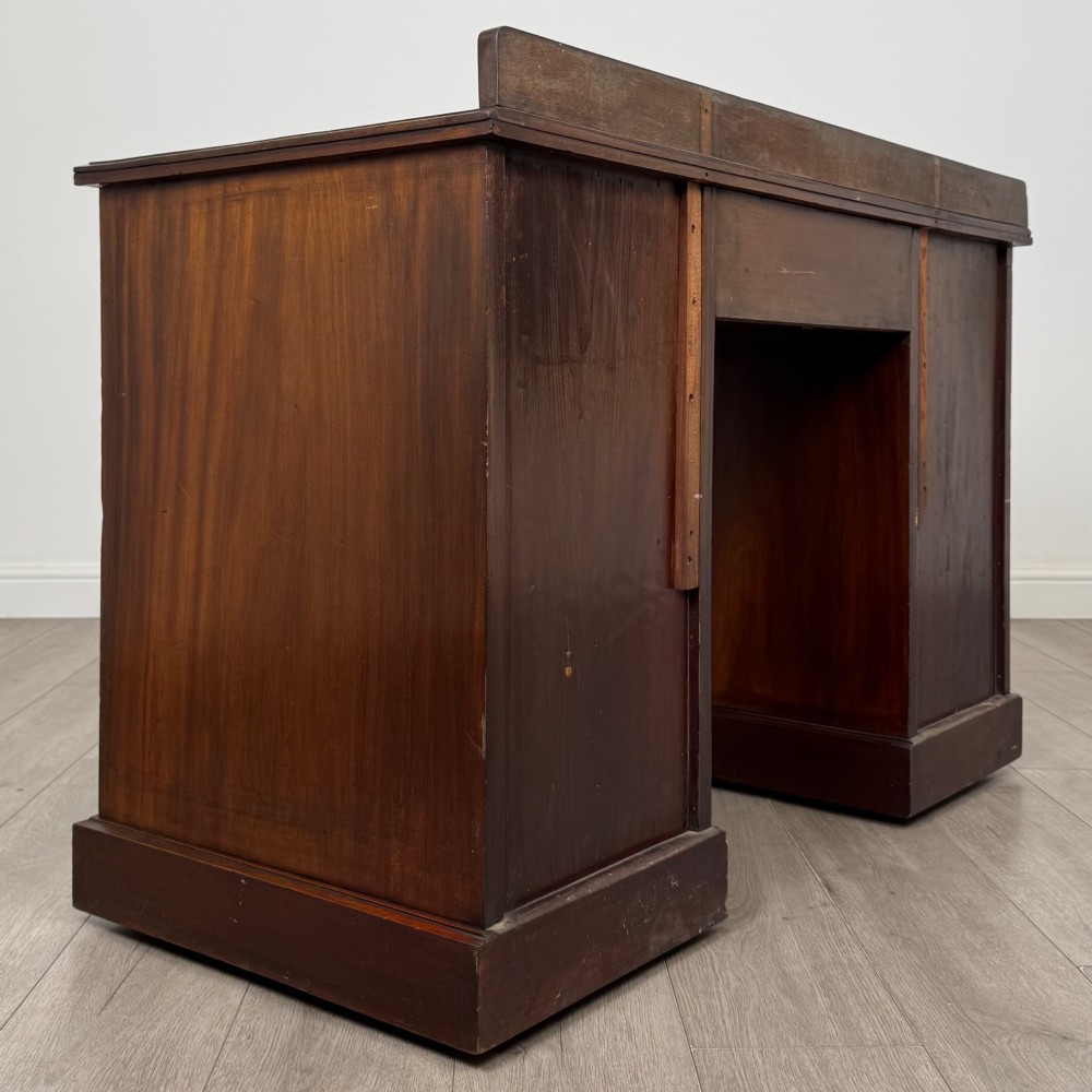 An antique Edwardian walnut pedestal desk featuring nine drawers with reeded panel details, brass drop handles, and a carved kneehole arch. View IV