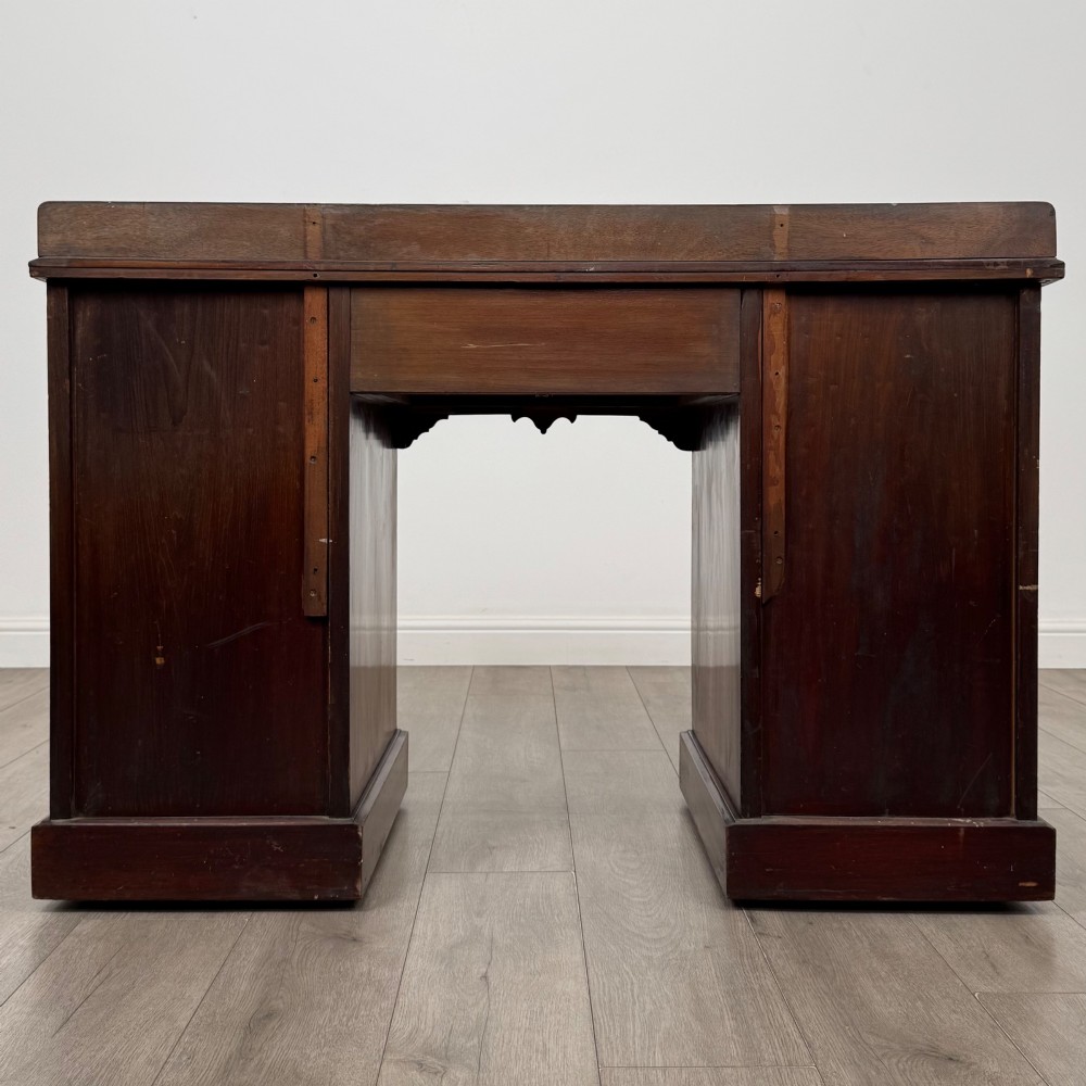 An antique Edwardian walnut pedestal desk featuring nine drawers with reeded panel details, brass drop handles, and a carved kneehole arch. View V