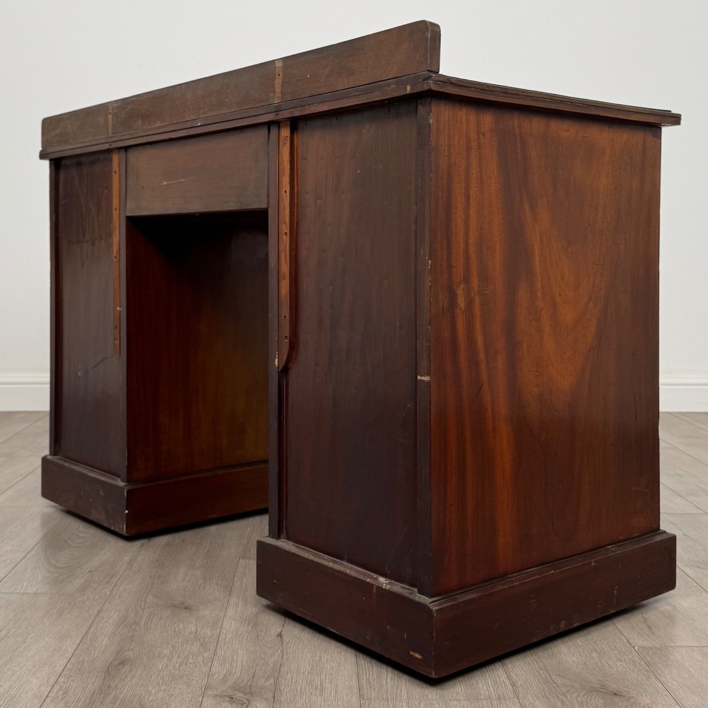 An antique Edwardian walnut pedestal desk featuring nine drawers with reeded panel details, brass drop handles, and a carved kneehole arch. View VI