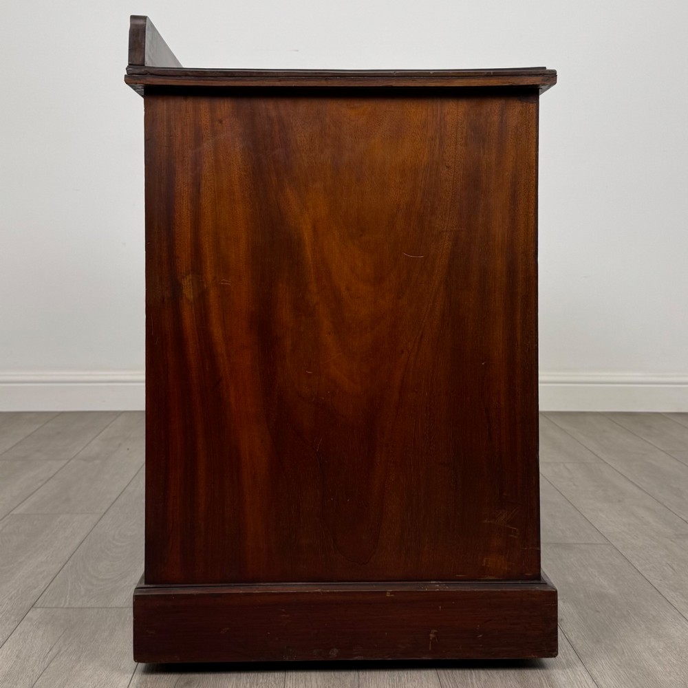 An antique Edwardian walnut pedestal desk featuring nine drawers with reeded panel details, brass drop handles, and a carved kneehole arch. View VII