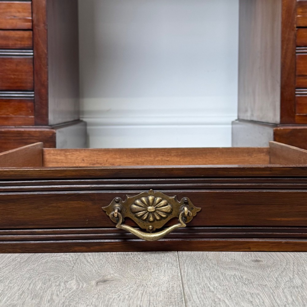 An antique Edwardian walnut pedestal desk featuring nine drawers with reeded panel details, brass drop handles, and a carved kneehole arch. View XI