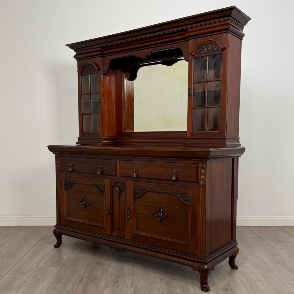 An Arts and Crafts dark mahogany sideboard featuring an upper mirrored superstructure flanked by leaded glass cabinet doors above lower drawers and carved cupboards. View III
