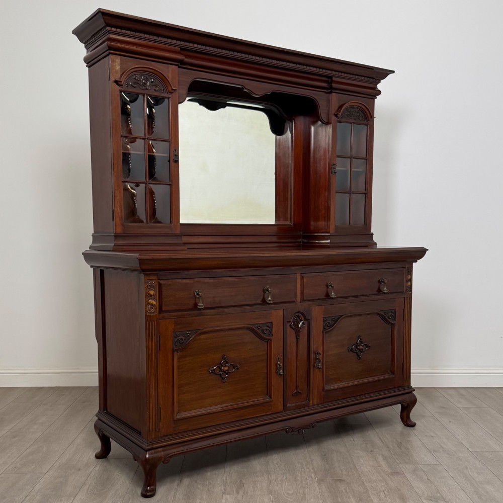An Arts and Crafts dark mahogany sideboard featuring an upper mirrored superstructure flanked by leaded glass cabinet doors above lower drawers and carved cupboards. View IX