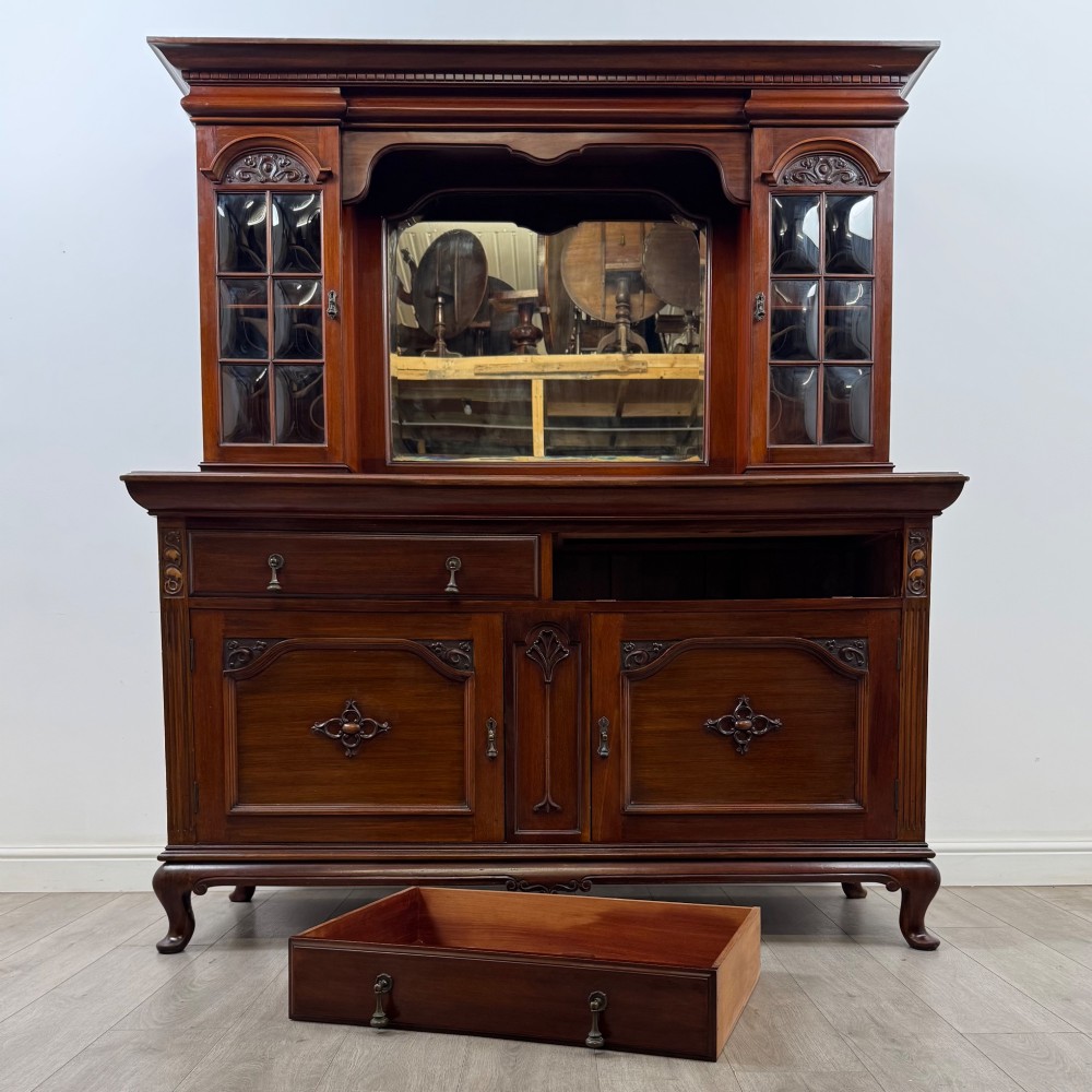 An Arts and Crafts dark mahogany sideboard featuring an upper mirrored superstructure flanked by leaded glass cabinet doors above lower drawers and carved cupboards. View XI