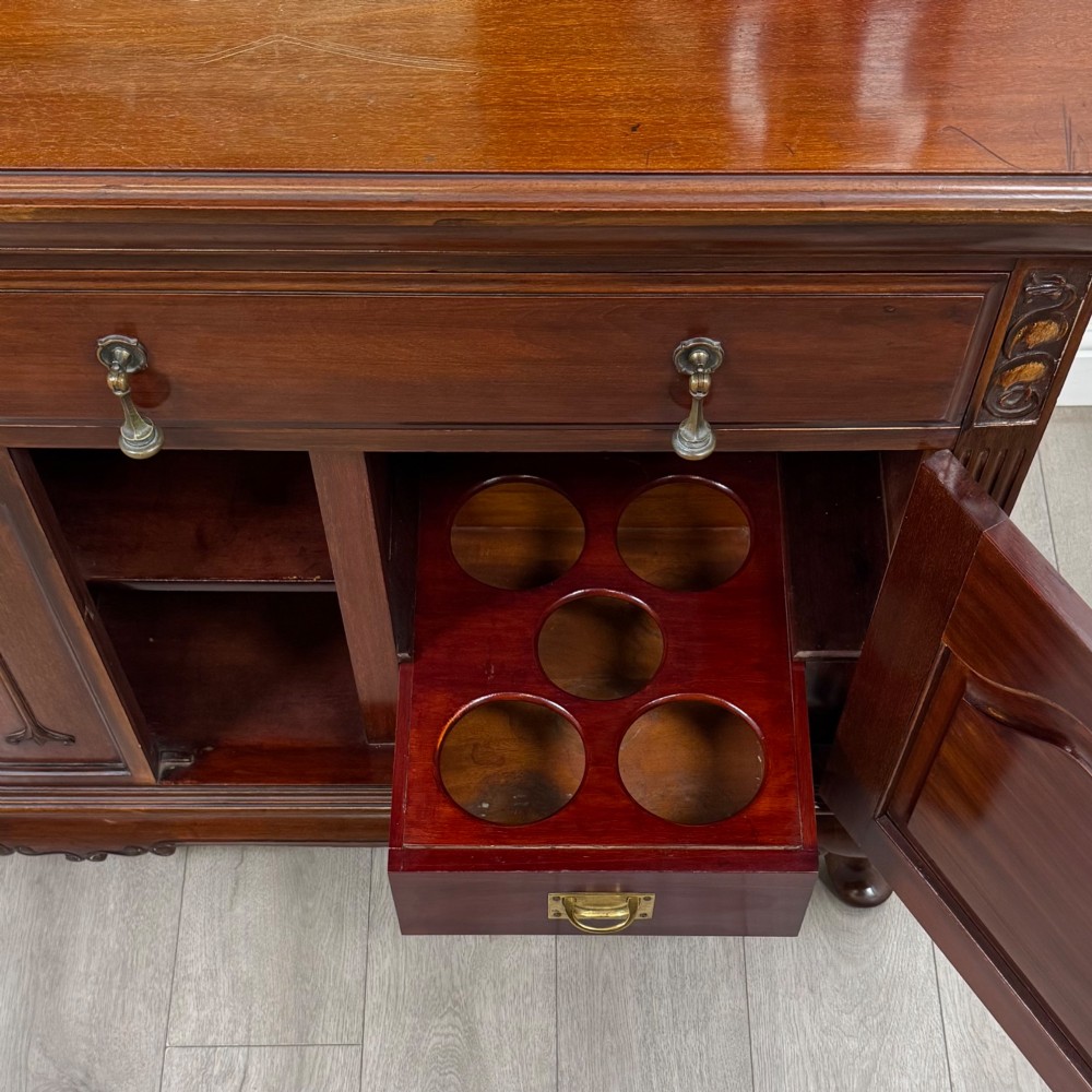 An Arts and Crafts dark mahogany sideboard featuring an upper mirrored superstructure flanked by leaded glass cabinet doors above lower drawers and carved cupboards. View XIII
