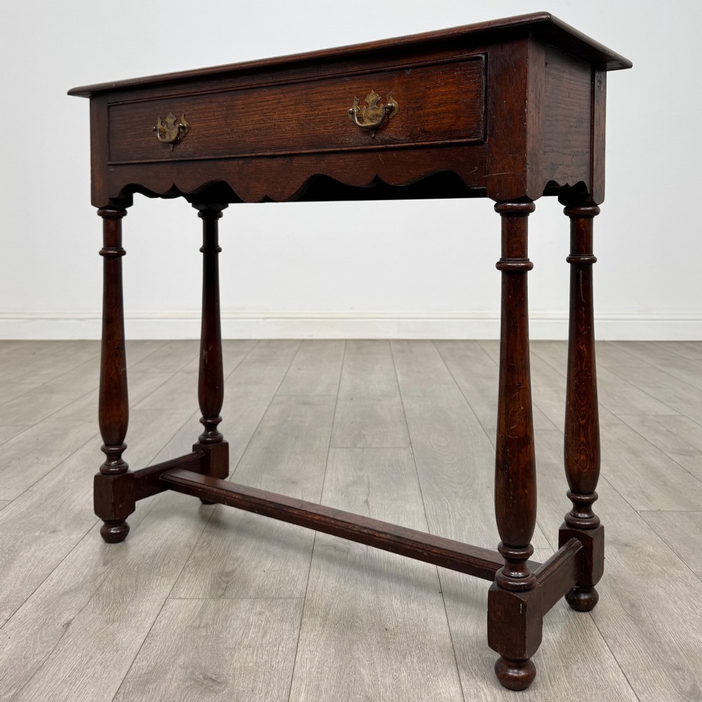 A dark oak side table featuring a single wide drawer with brass drop handles, a scalloped apron, turned legs, and lower stretchers. View II