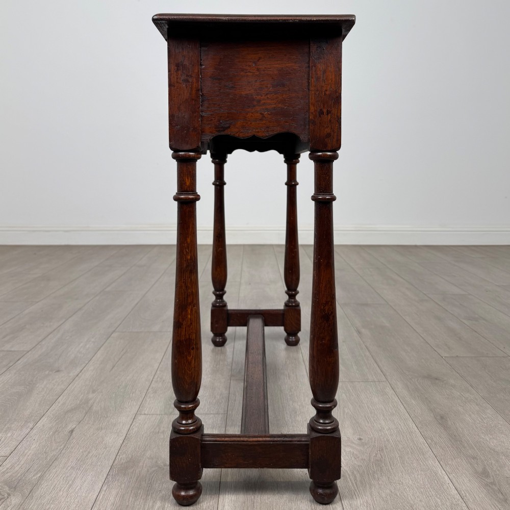 A dark oak side table featuring a single wide drawer with brass drop handles, a scalloped apron, turned legs, and lower stretchers. View III