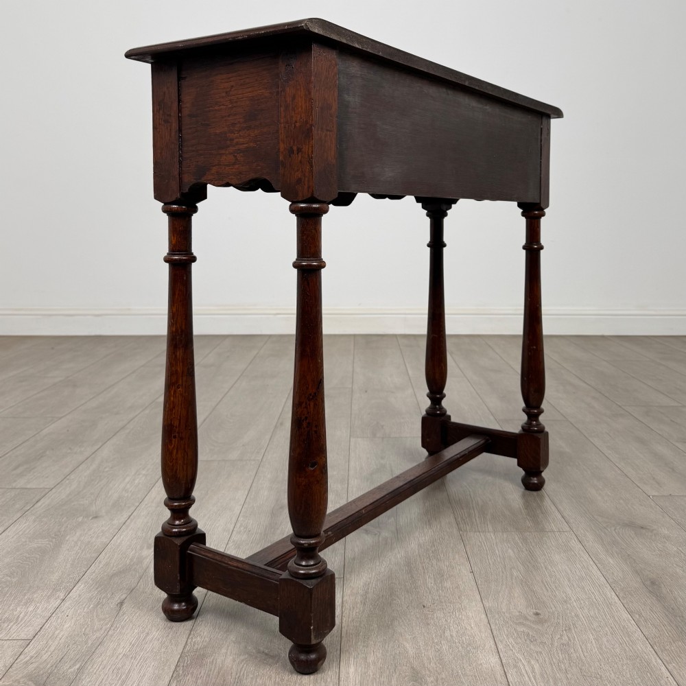 A dark oak side table featuring a single wide drawer with brass drop handles, a scalloped apron, turned legs, and lower stretchers. View IV