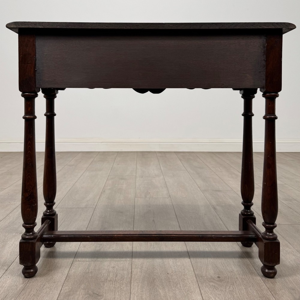 A dark oak side table featuring a single wide drawer with brass drop handles, a scalloped apron, turned legs, and lower stretchers. View V