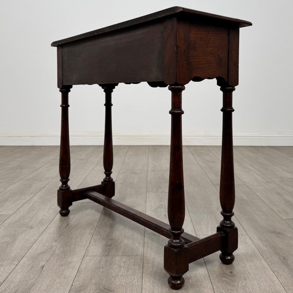 A dark oak side table featuring a single wide drawer with brass drop handles, a scalloped apron, turned legs, and lower stretchers. View VI
