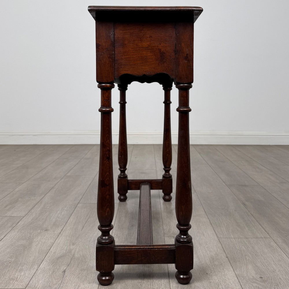 A dark oak side table featuring a single wide drawer with brass drop handles, a scalloped apron, turned legs, and lower stretchers. View VII
