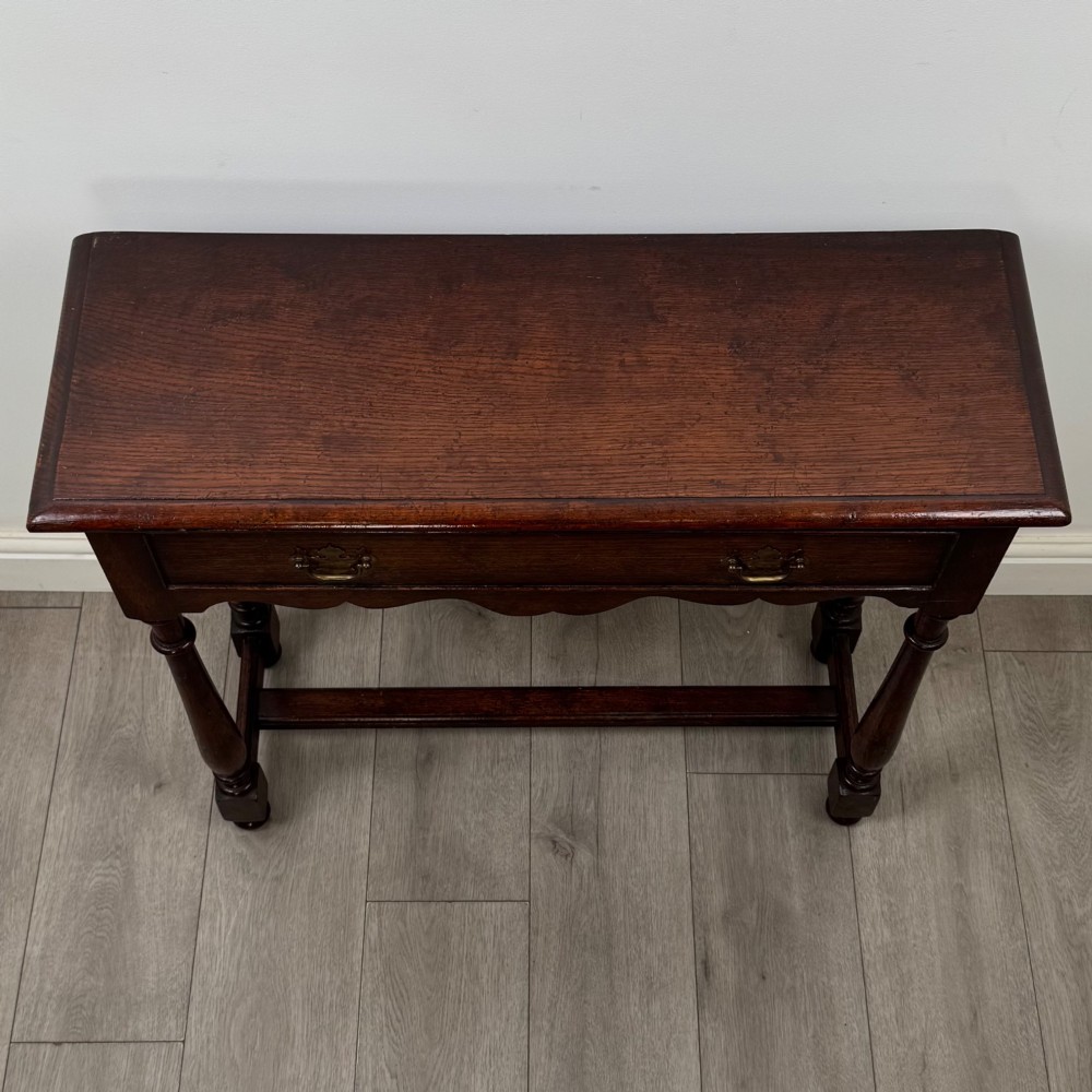 A dark oak side table featuring a single wide drawer with brass drop handles, a scalloped apron, turned legs, and lower stretchers. View IX