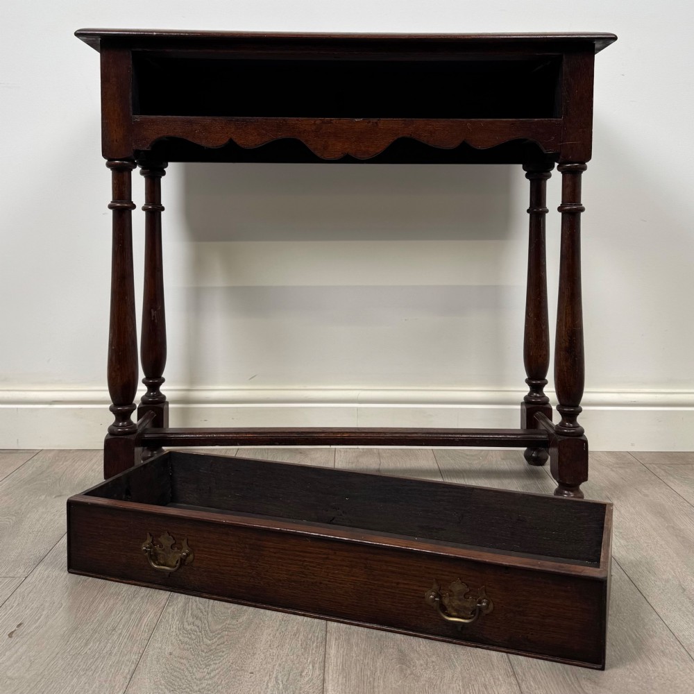A dark oak side table featuring a single wide drawer with brass drop handles, a scalloped apron, turned legs, and lower stretchers. View X