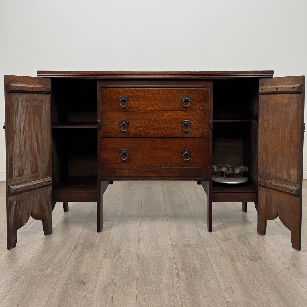 A dark oak Gothic Revival sideboard featuring three central drawers with metal drop ring handles, flanked by two carved tracery panel doors with decorative iron latches. View II