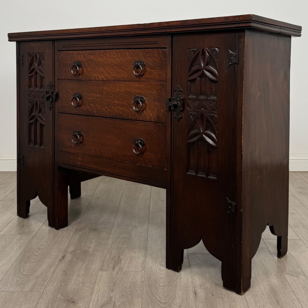 A dark oak Gothic Revival sideboard featuring three central drawers with metal drop ring handles, flanked by two carved tracery panel doors with decorative iron latches. View III