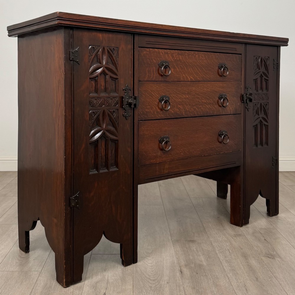 A dark oak Gothic Revival sideboard featuring three central drawers with metal drop ring handles, flanked by two carved tracery panel doors with decorative iron latches. View IX