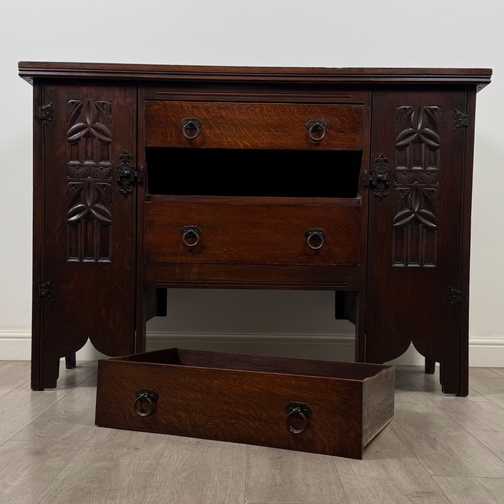 A dark oak Gothic Revival sideboard featuring three central drawers with metal drop ring handles, flanked by two carved tracery panel doors with decorative iron latches. View XI