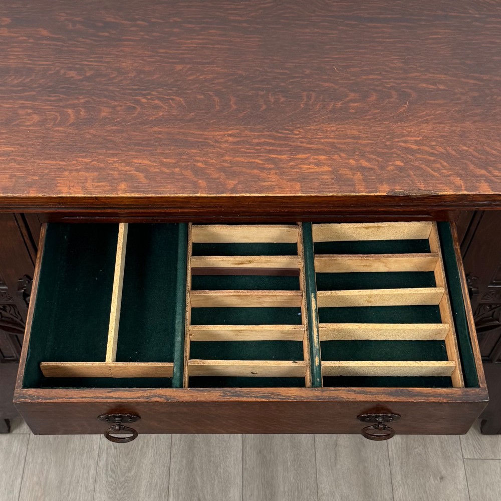 A dark oak Gothic Revival sideboard featuring three central drawers with metal drop ring handles, flanked by two carved tracery panel doors with decorative iron latches. View XIII