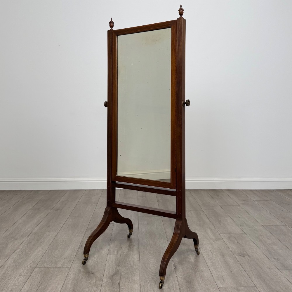 An Edwardian mahogany full-length cheval mirror featuring a rectangular tilting glass frame supported by a wooden upright stand with finials and splayed feet on brass castors.