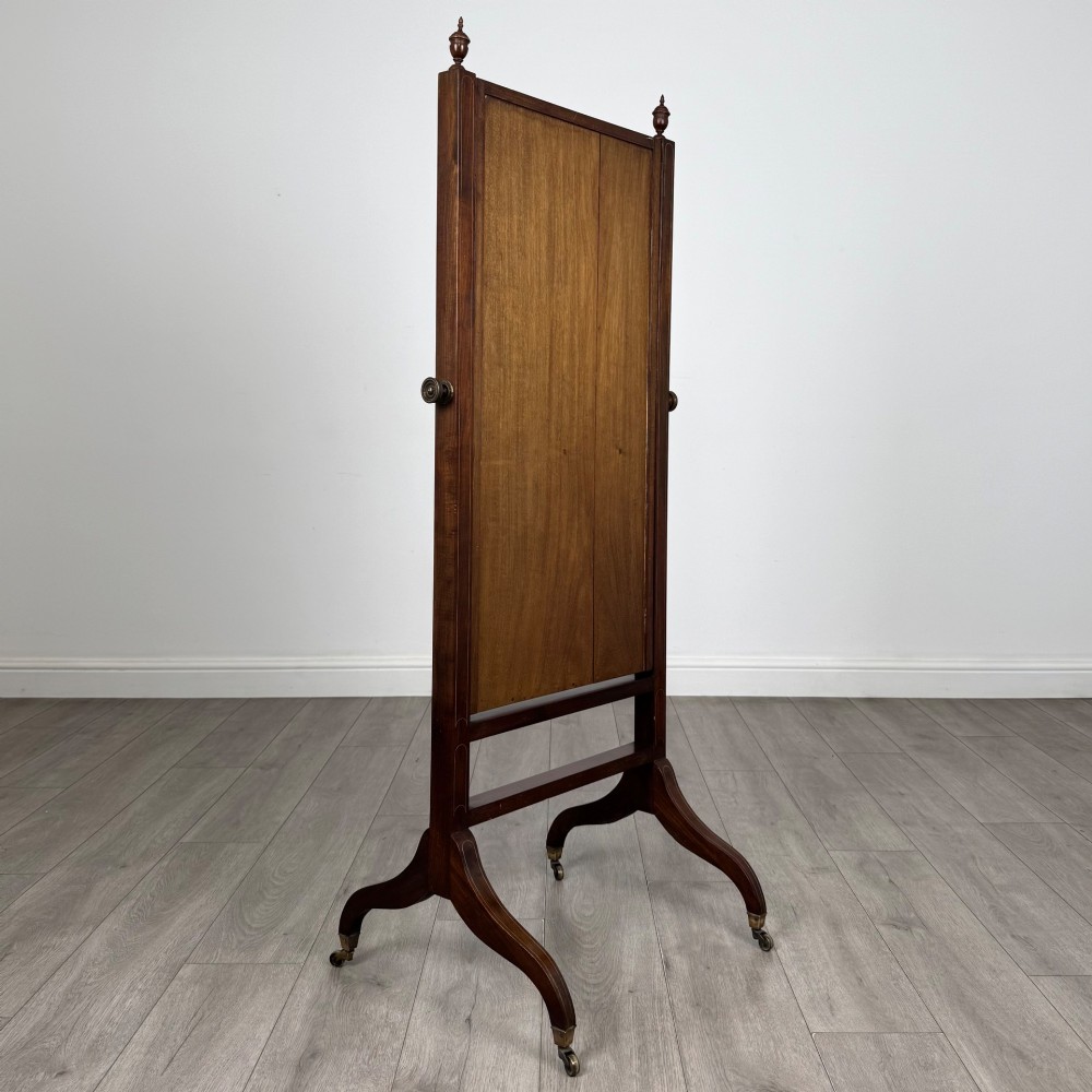 An Edwardian mahogany full-length cheval mirror featuring a rectangular tilting glass frame supported by a wooden upright stand with finials and splayed feet on brass castors. View IV