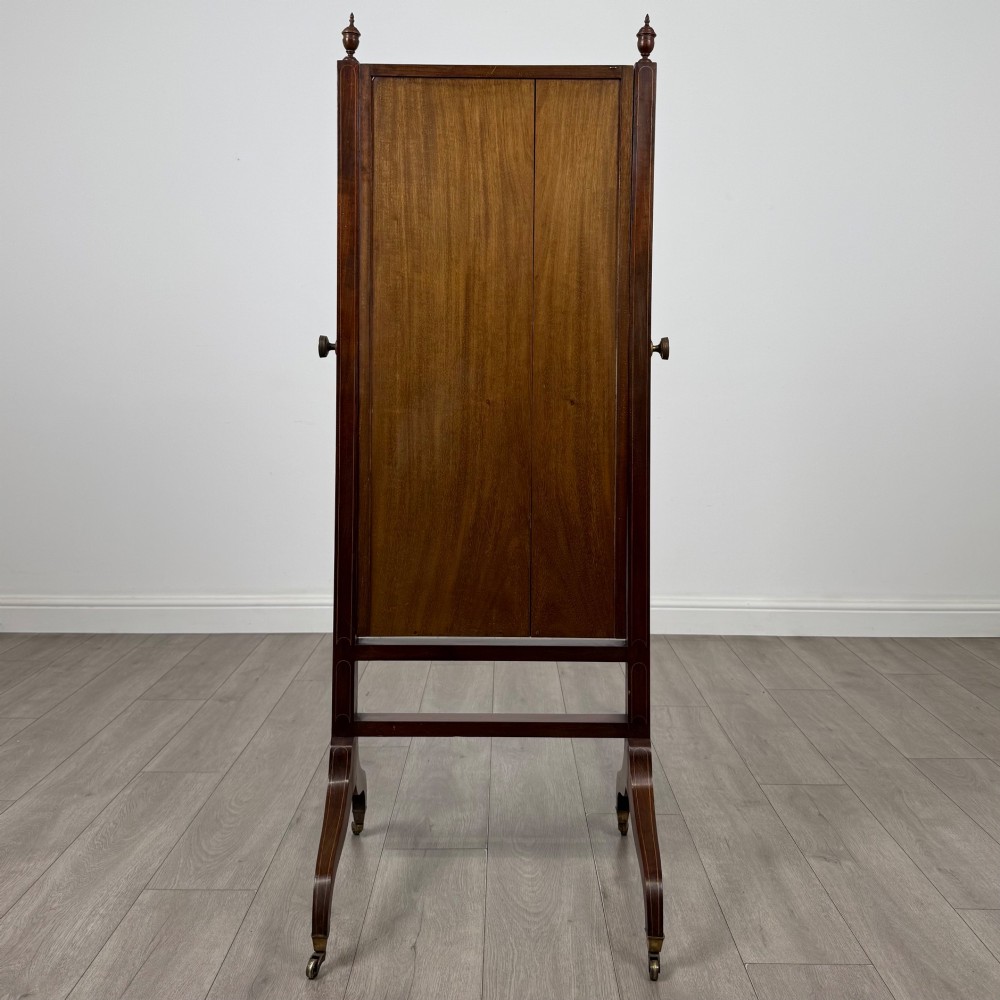 An Edwardian mahogany full-length cheval mirror featuring a rectangular tilting glass frame supported by a wooden upright stand with finials and splayed feet on brass castors. View V