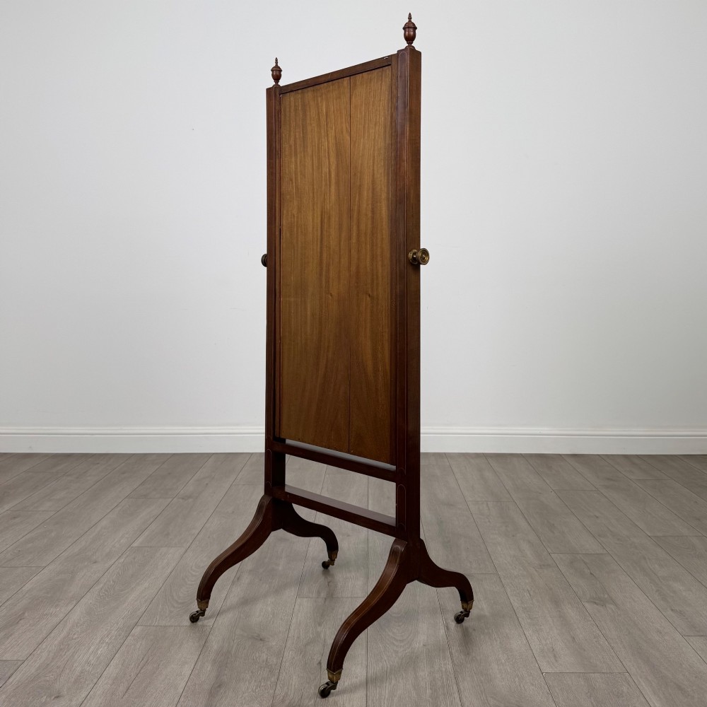 An Edwardian mahogany full-length cheval mirror featuring a rectangular tilting glass frame supported by a wooden upright stand with finials and splayed feet on brass castors. View VI