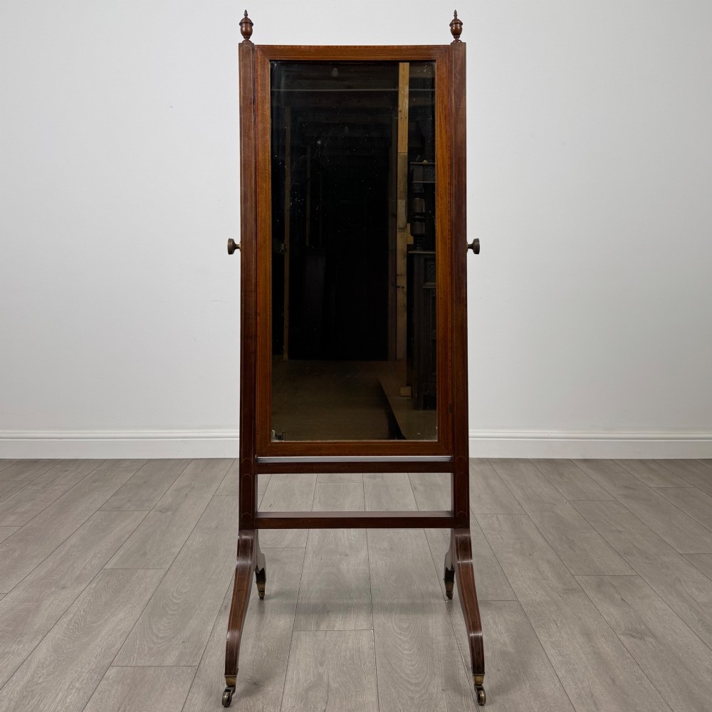 An Edwardian mahogany full-length cheval mirror featuring a rectangular tilting glass frame supported by a wooden upright stand with finials and splayed feet on brass castors. View X