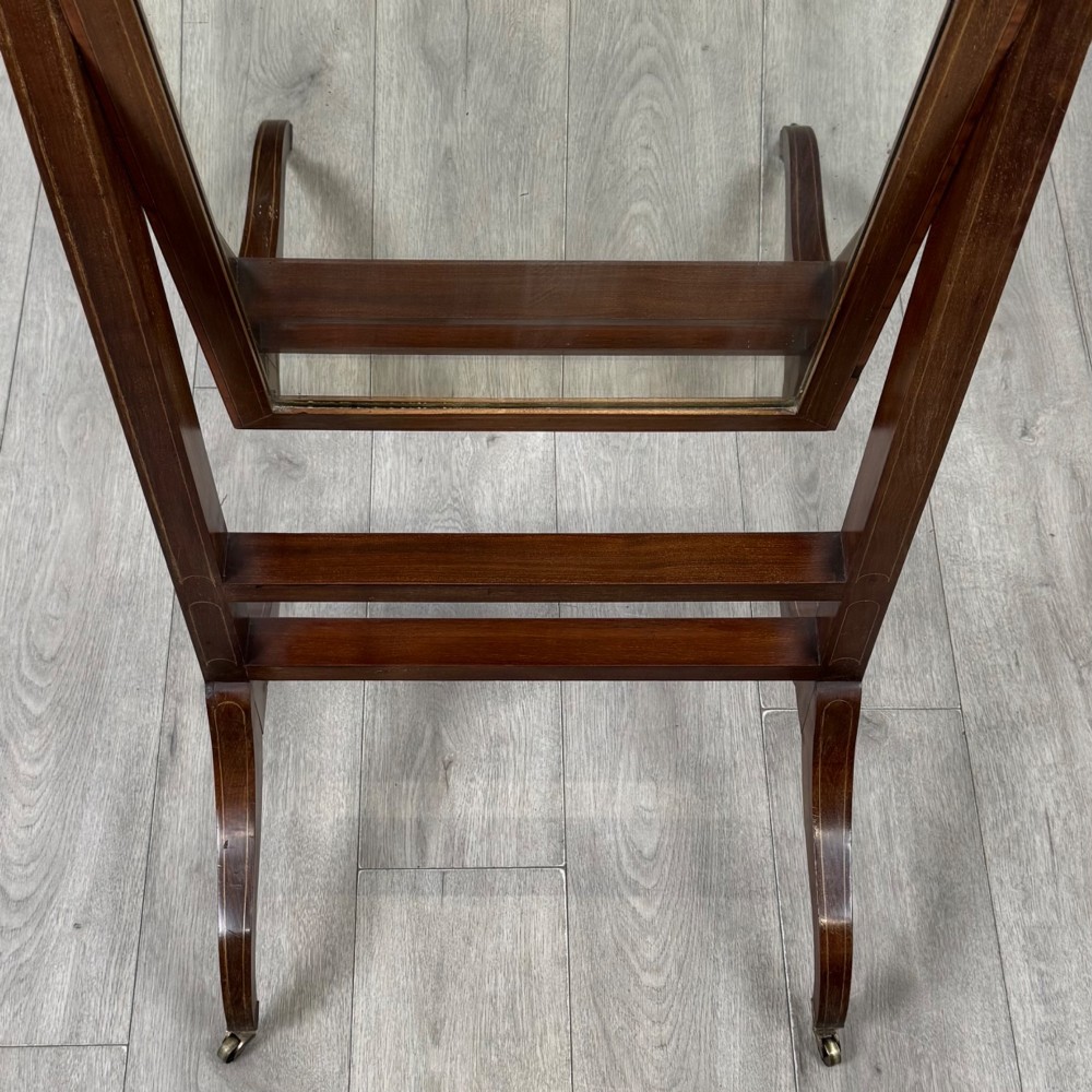 An Edwardian mahogany full-length cheval mirror featuring a rectangular tilting glass frame supported by a wooden upright stand with finials and splayed feet on brass castors. View XI