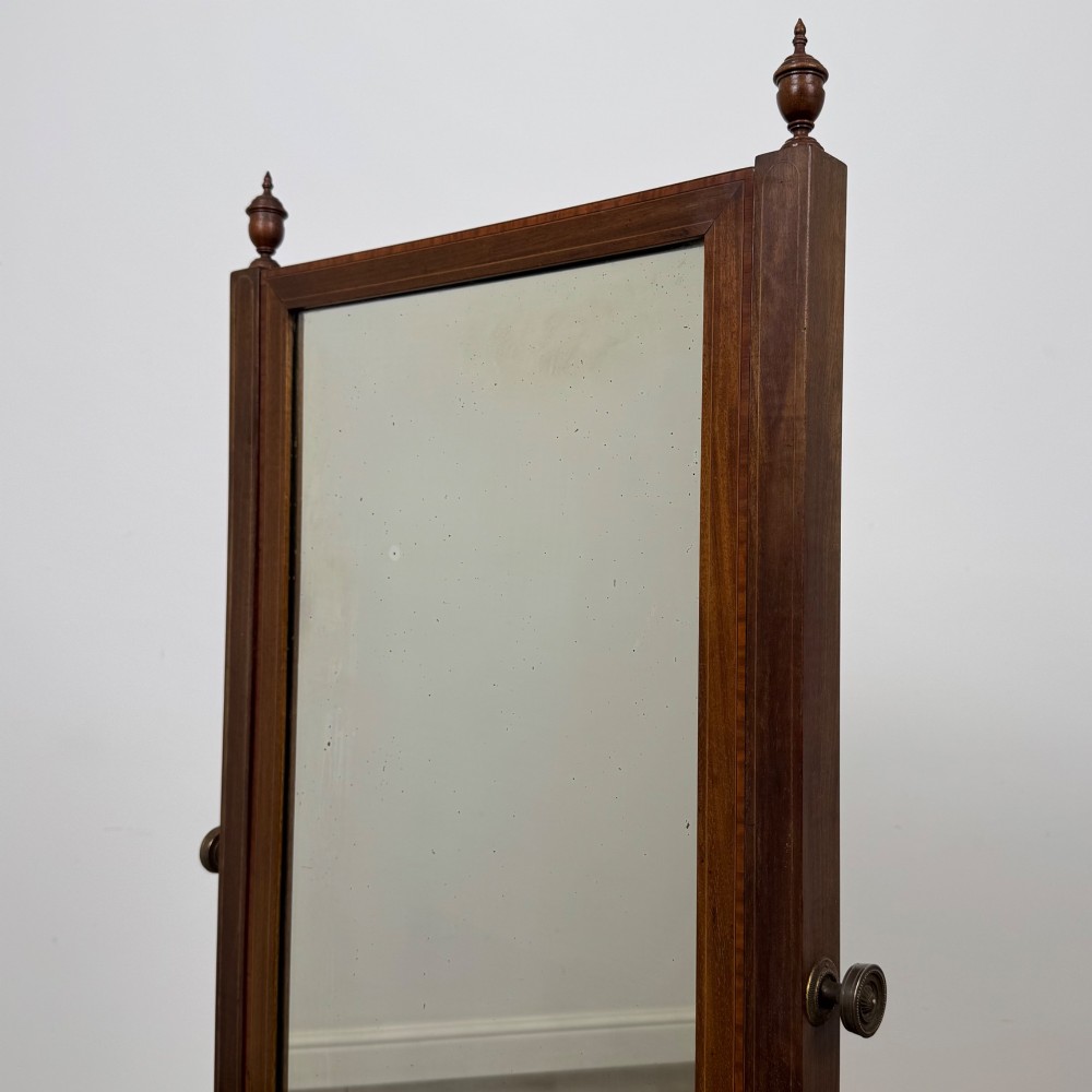 An Edwardian mahogany full-length cheval mirror featuring a rectangular tilting glass frame supported by a wooden upright stand with finials and splayed feet on brass castors. View XII