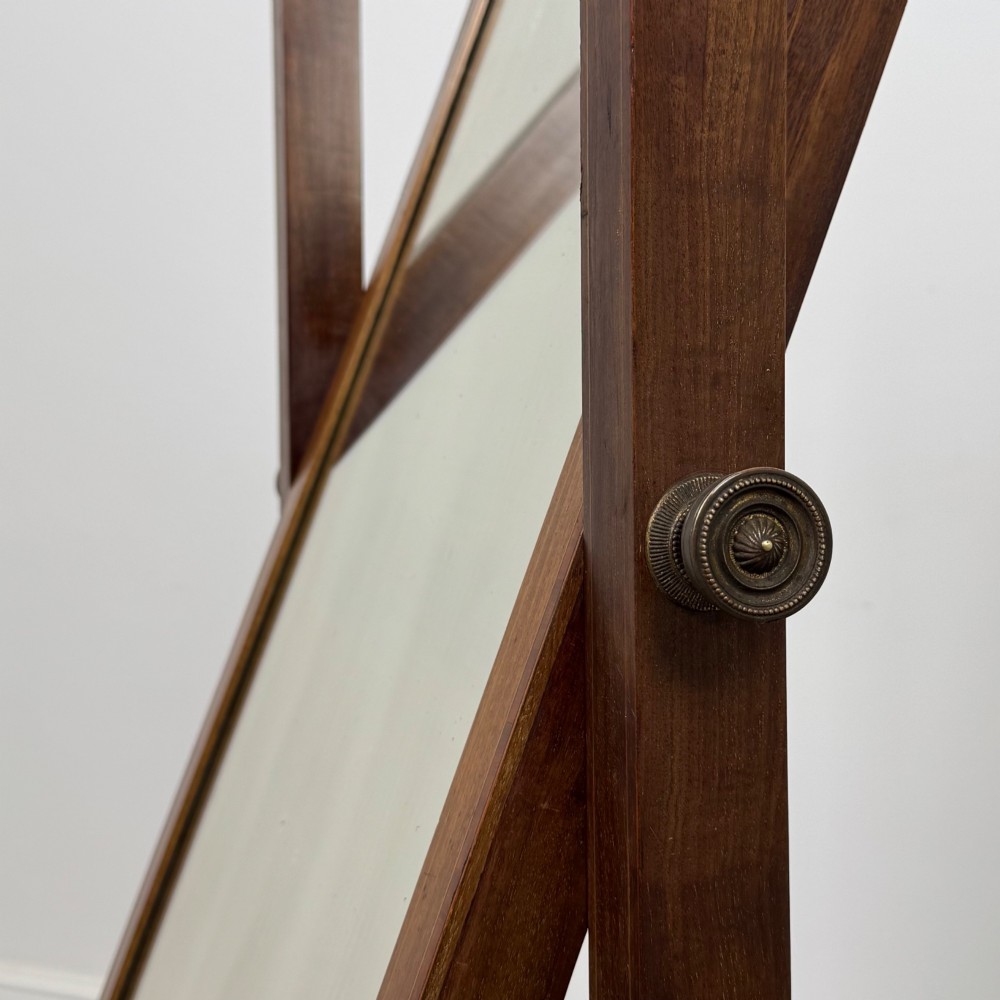 An Edwardian mahogany full-length cheval mirror featuring a rectangular tilting glass frame supported by a wooden upright stand with finials and splayed feet on brass castors. View XIII