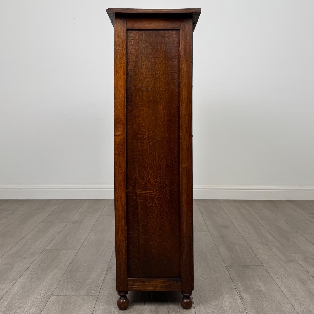 An Edwardian warm brown oak display cabinet featuring twin leaded glass doors with a geometric pattern, interior wooden shelves, and rounded bun feet. View IV