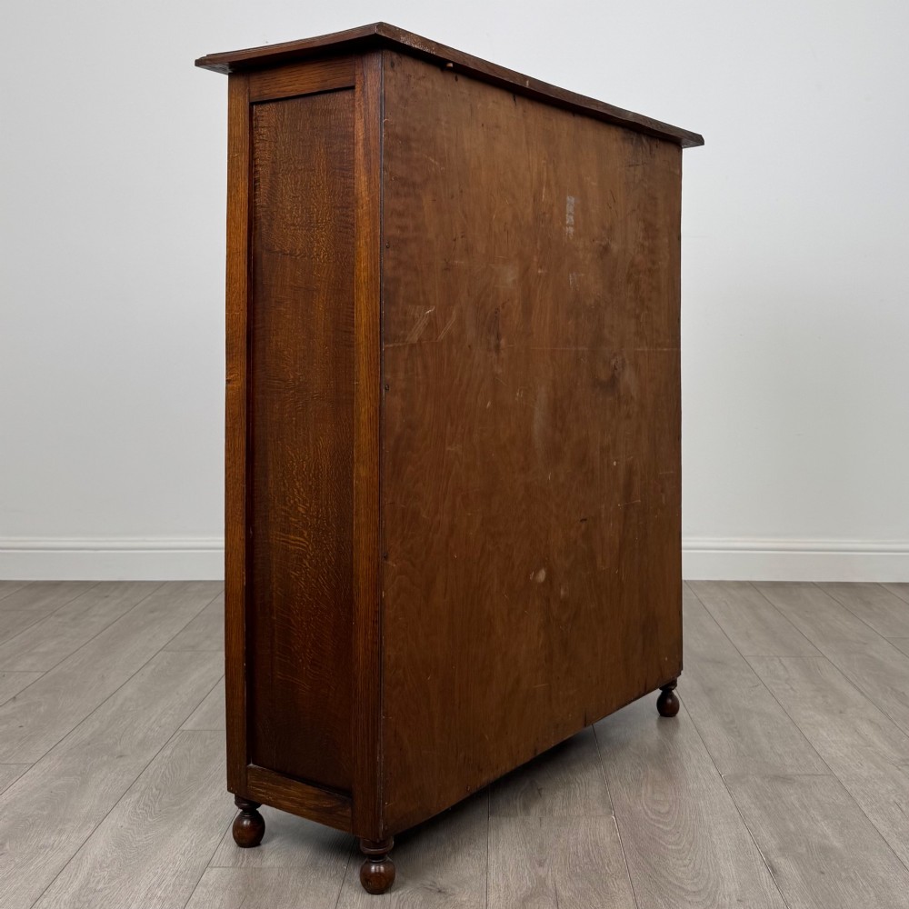 An Edwardian warm brown oak display cabinet featuring twin leaded glass doors with a geometric pattern, interior wooden shelves, and rounded bun feet. View V