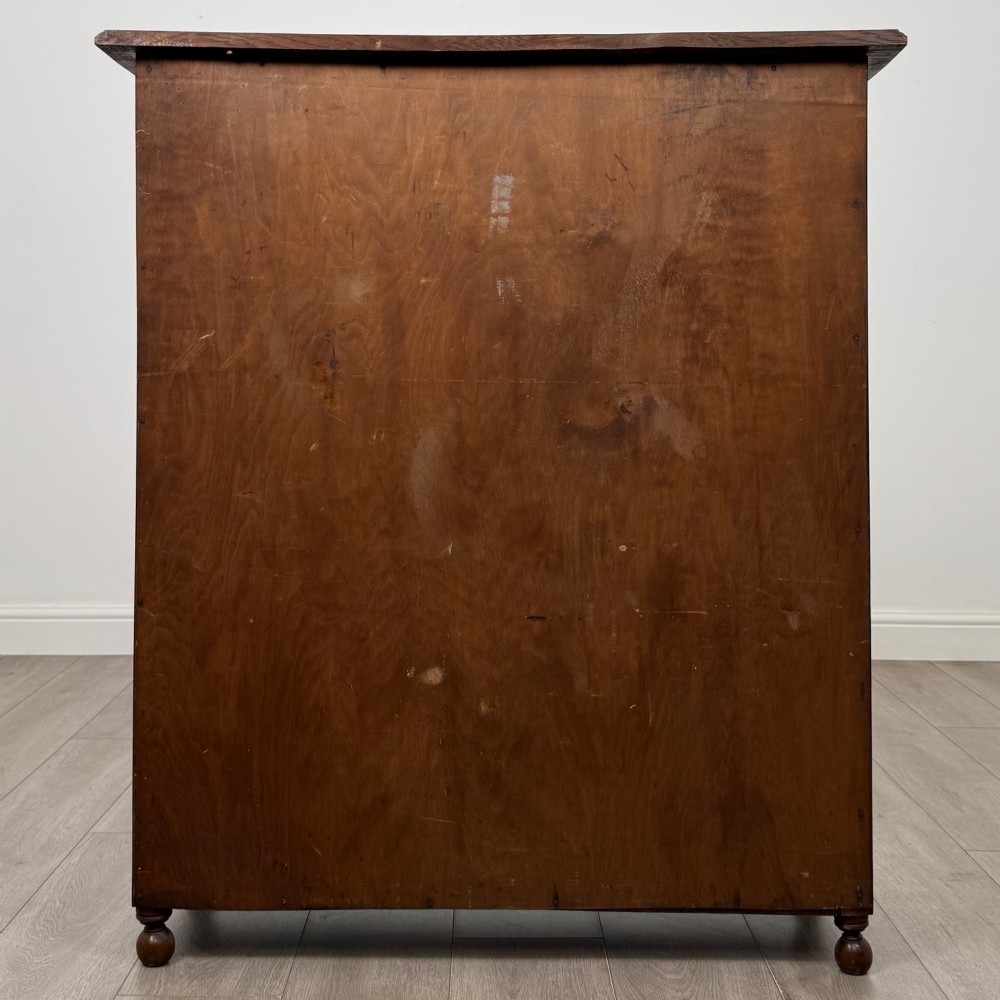 An Edwardian warm brown oak display cabinet featuring twin leaded glass doors with a geometric pattern, interior wooden shelves, and rounded bun feet. View VI