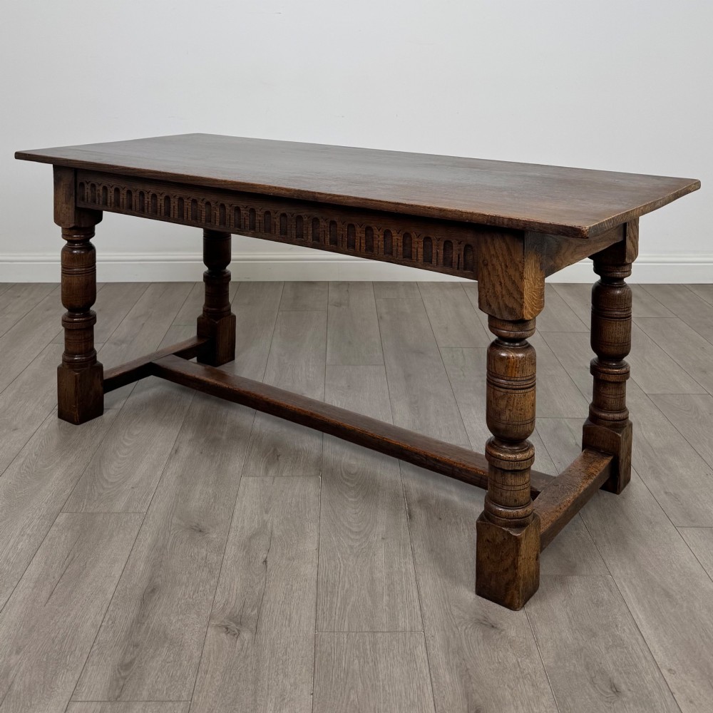 A dark oak rectangular refectory dining table featuring a carved arch frieze, four turned legs, and a low H-stretcher.