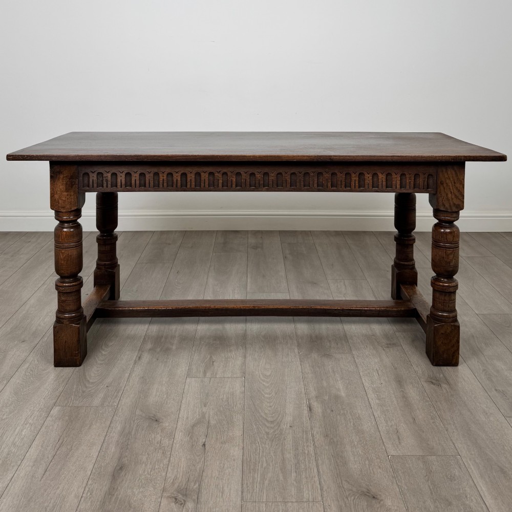 A dark oak rectangular refectory dining table featuring a carved arch frieze, four turned legs, and a low H-stretcher. View II