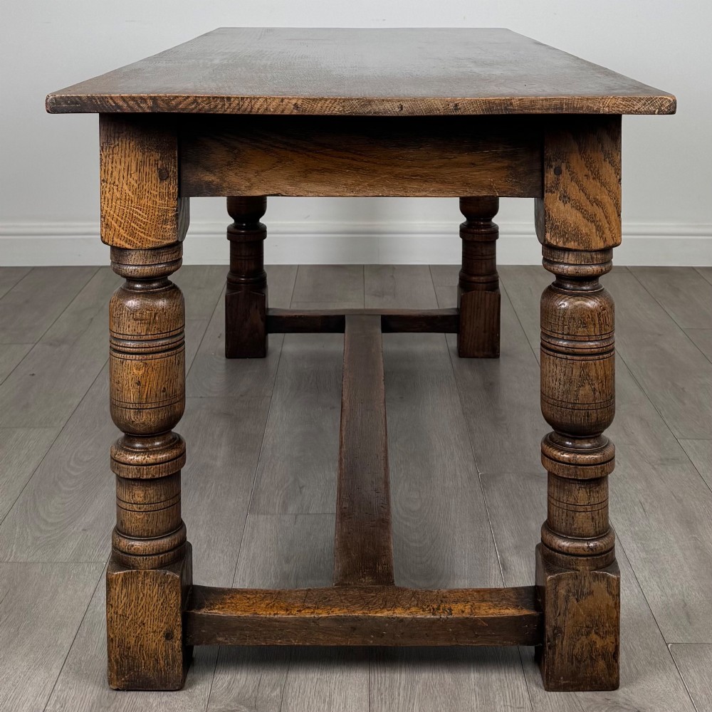 A dark oak rectangular refectory dining table featuring a carved arch frieze, four turned legs, and a low H-stretcher. View III