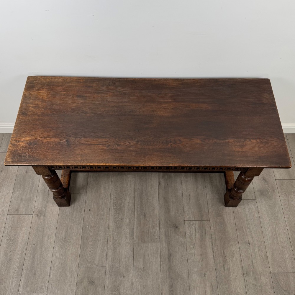 A dark oak rectangular refectory dining table featuring a carved arch frieze, four turned legs, and a low H-stretcher. View IV