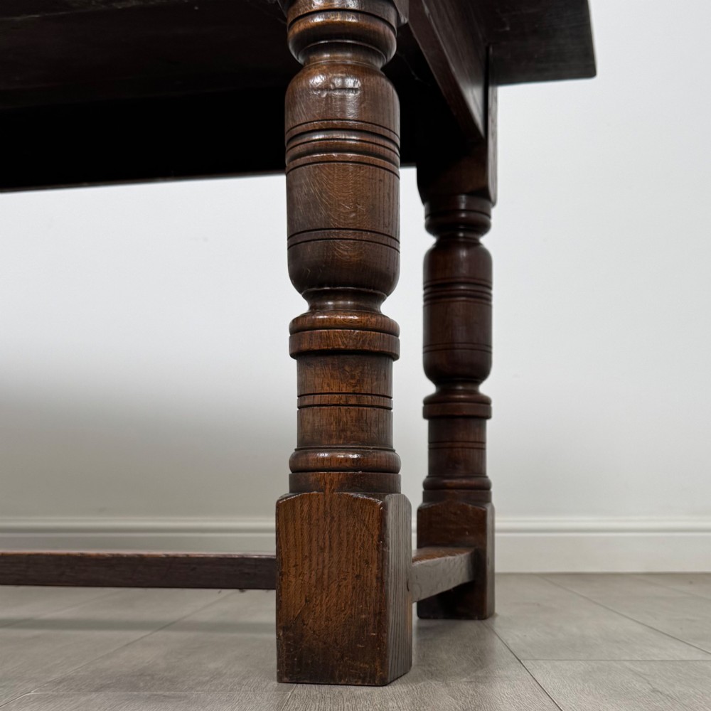 A dark oak rectangular refectory dining table featuring a carved arch frieze, four turned legs, and a low H-stretcher. View VI