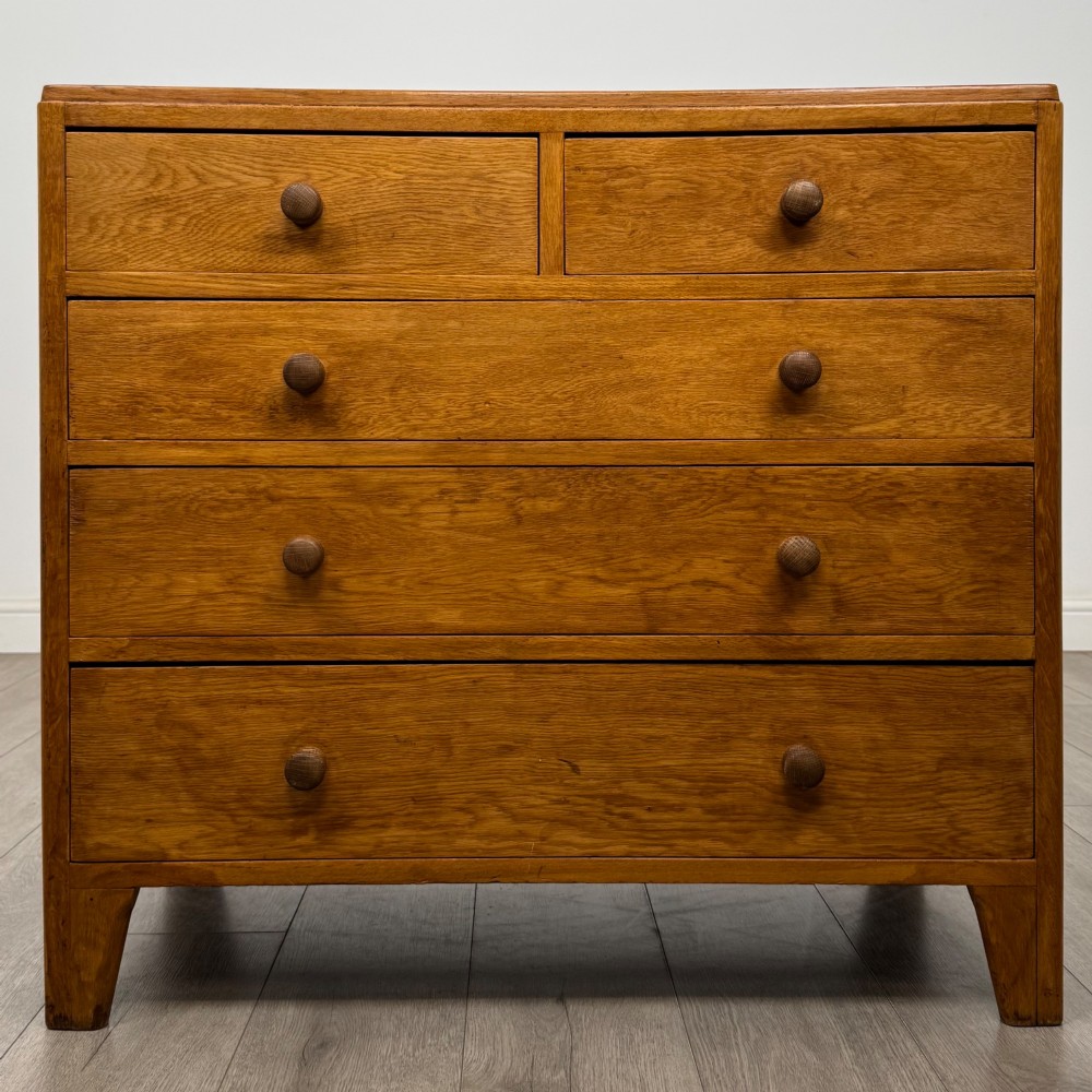 An antique golden oak chest of drawers featuring two short drawers above three long drawers with turned wooden knobs.